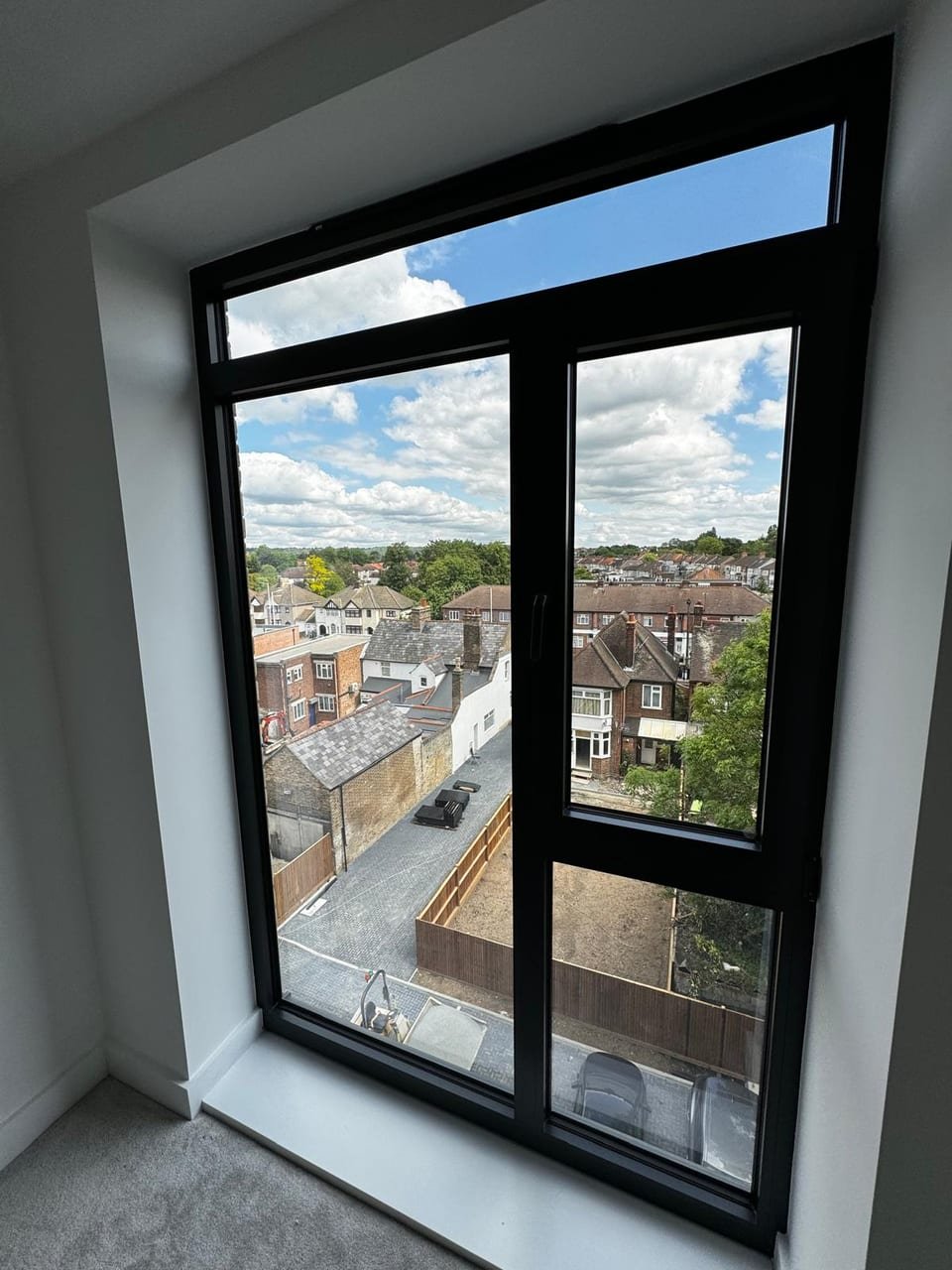 Tilt-and-turn window in a finished bedroom, the vent held open against a blue sky above North London rooftops