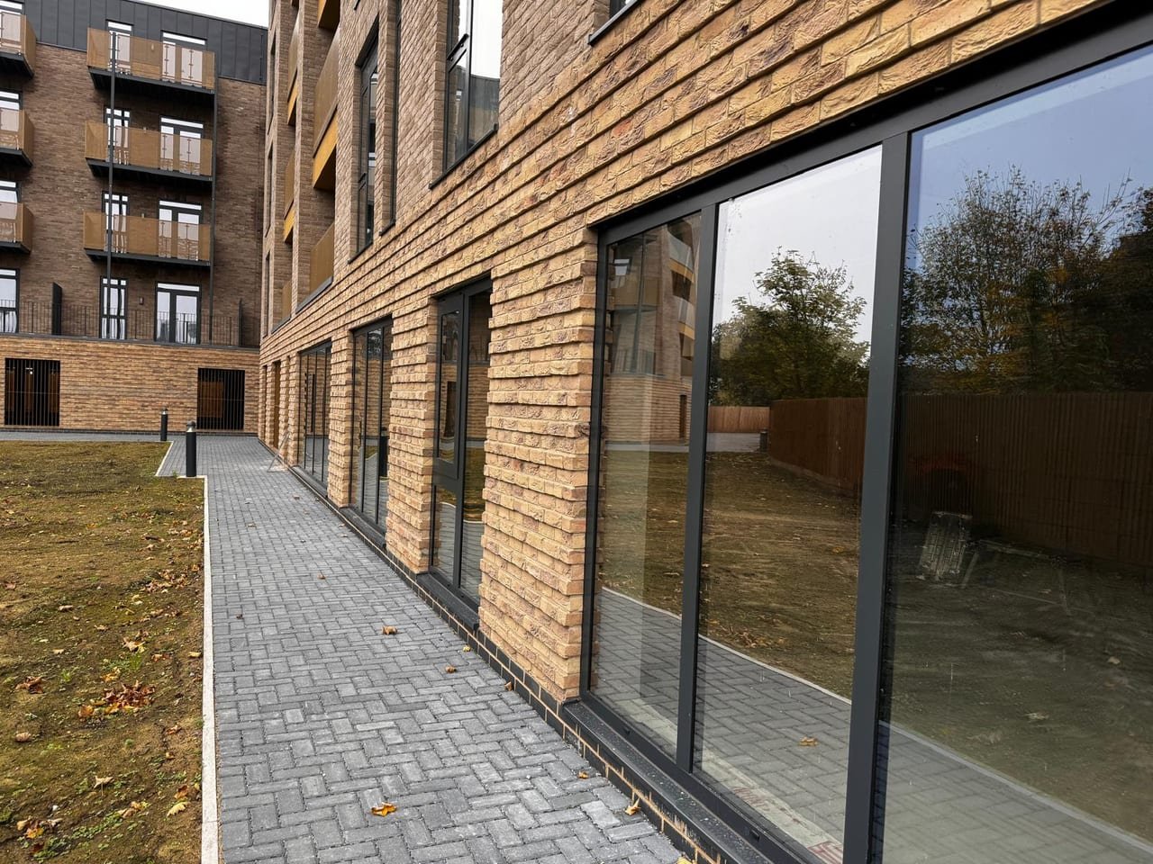 Run of full-height aluminium glazing along a ground-floor commercial elevation reflecting the courtyard