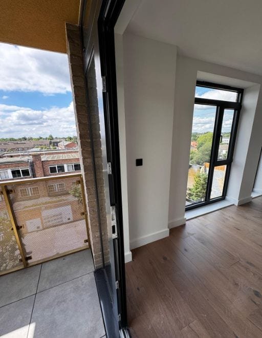 Aluminium door standing open at the threshold of a finished apartment, looking out towards a neighbouring brick building