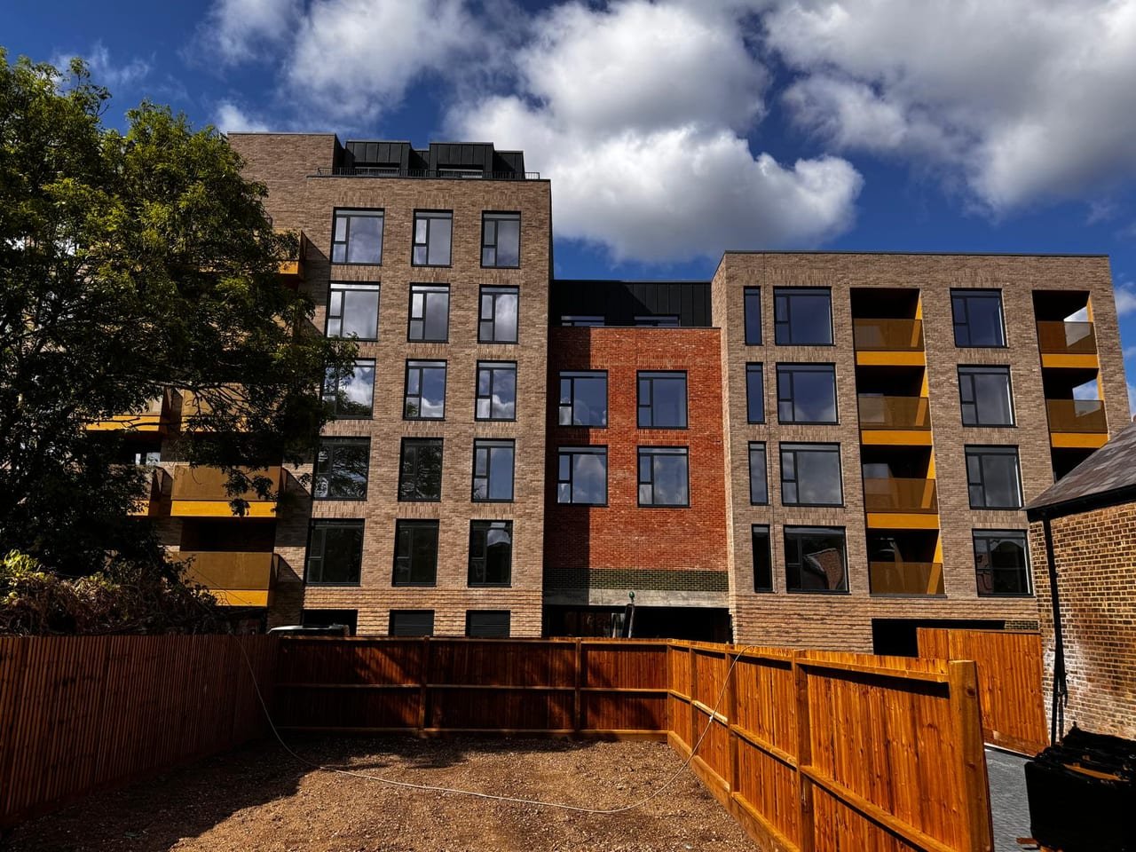 Sunlit brick elevation of a completed London apartment development with anthracite aluminium windows and gold balcony screens