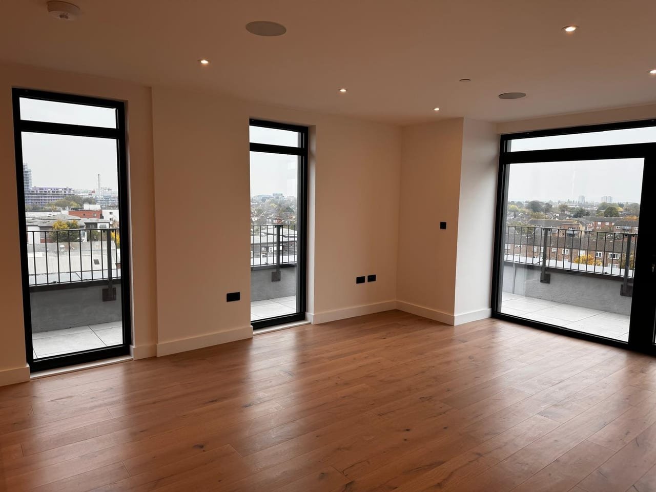 Finished apartment living space with three full-height aluminium glazed doors opening onto a balcony